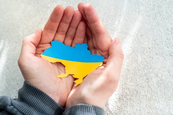Hands holding the national flag of Ukraine in the shape of the b